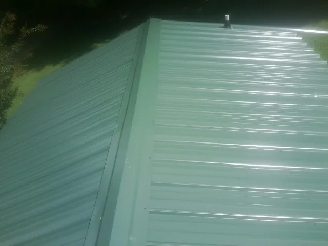 New green metal panels meeting at the ridge of a roof — Flat Roof Repair work by our crew in Holland Patent