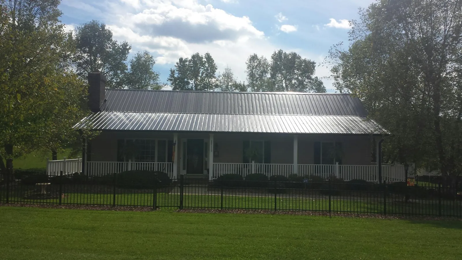 Gray metal roof on a brick ranch with a full width front porch — Gutter Guard Installation work by our crew in Holland Patent