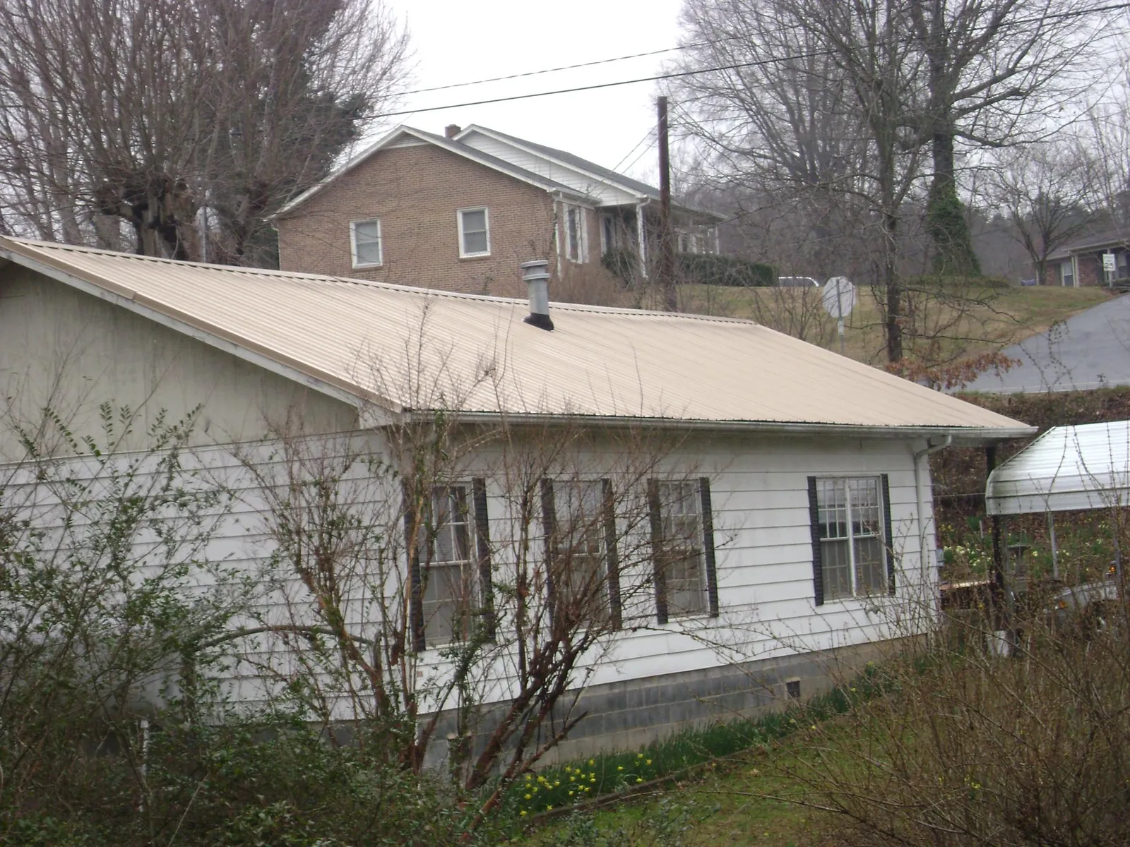 Tan metal roof on a white sided house set into a hillside — Commercial Roofing by Roofing Brothers in Holland Patent