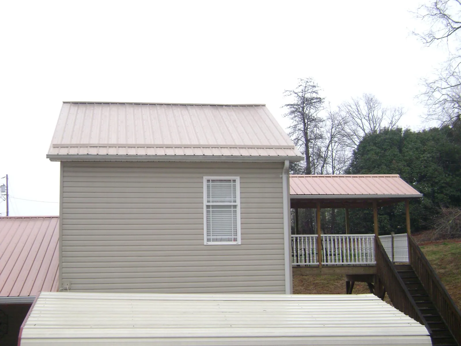 Tan metal roofs on a two story addition and attached porch, from a Roof Replacement job in Holland Patent